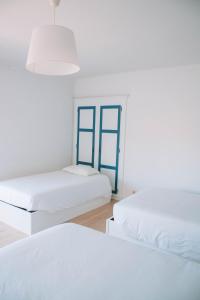 Duas camas num quarto branco com janelas azuis em Arca Nova Guest House & Hostel Caminha em Caminha