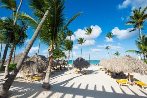 a beach with straw umbrellas and chairs and palm trees at Luxury Private Villas with Pool Beach BBQ in Punta Cana