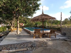 a pool with benches and a straw umbrella at Lanta Dareen Garden Home in Ko Lanta