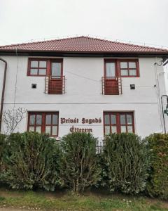 biały dom z czerwonymi oknami i krzakami z przodu w obiekcie Privát Fogadó és Étterem w mieście Bükkszentkereszt