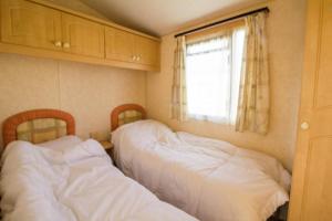 2 camas en una habitación pequeña con ventana en 6 Berth Caravan For Hire, Minutes From A Stunning Beach In Norfolk! Ref 21036f en Heacham