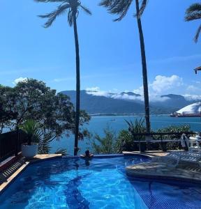uma piscina com palmeiras e vista para a água em Pousada Fruto do Mar em Ilhabela