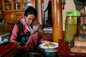 een vrouw op de vloer met een bord eten bij Likir Pottery Homestay - Likir Village - Sham Valley in Leh