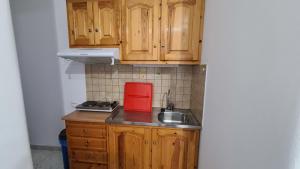 una pequeña cocina con armarios de madera y un aparato rojo en Amarandos Studios - Rooms & Apartments, en Marantochori