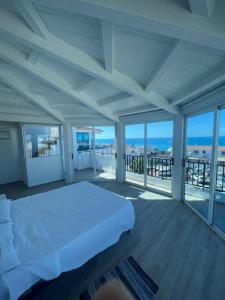 a white bedroom with a bed and large windows at Ale Mare - Attico con idromassaggio vista mare in Marina di Ragusa