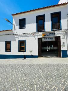 een wit gebouw met een deur en een geplaveide straat bij Só Mar in Vila Nova de Milfontes