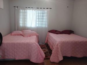 two beds in a room with pink sheets and a window at Pousada Guaíra in Guaíra