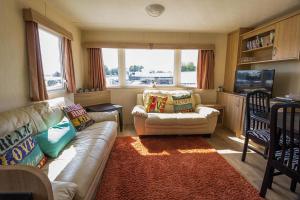 a living room with a couch and a television at 6 Berth Caravan For Hire With Decking At Manor Park In Norfolk Ref 23017s in Hunstanton