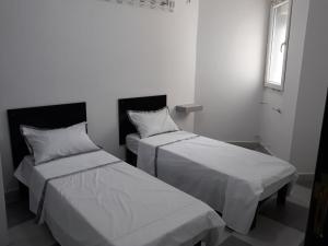two beds in a room with white sheets and a window at Immeuble THALA Tigzirt appart 90m2 in Tigzirt