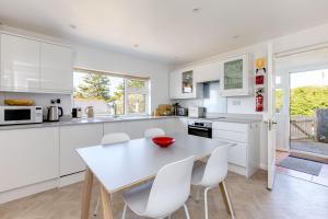 a white kitchen with a table and white chairs at Bella Vista in Polzeath +12 photos