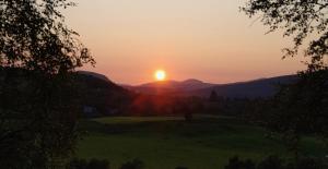 a sunset over a green field with mountains in the background at Ivy Cottage Bed and Breakfast in Braemar