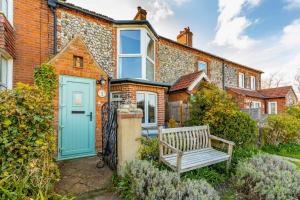 una casa con una puerta azul y un banco en St Josephs Cottage, en West Runton