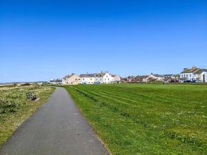 a path through a field with houses in the background at Seascape Cottage in Allonby