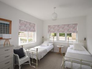 a bedroom with two beds and a chair and two windows at Nyth Y Fran in Abersoch
