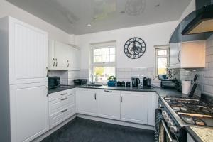 Cosy & Central 2BD Apartment Milngavie, Glasgow في ميلنغافي: مطبخ بدولاب بيضاء وموقد