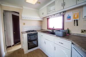 a kitchen with white cabinets and a sink and a stove at Dog Friendly 6 Berth Static Caravan By The Beach In Hunstanton Ref 13008l in Hunstanton