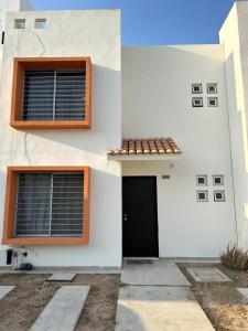 uma casa branca com uma porta preta e janelas em Relajante casa con alberca & auto check-in em Mazatlán
