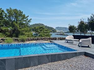 a swimming pool with two chairs and a table next to the water at Luxury Pool Villa, Villecot in Seogwipo