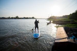 a man is standing on a paddle board in the water at Baan GoLite Ko Kret - บ้านโกไล้เกาะเกร็ด in Nonthaburi