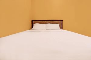 1 cama con sábanas blancas y cabecero de madera en SPOT ON 92523 Homestay Pasir Padi Permai Syariah, en Pangkalpinang