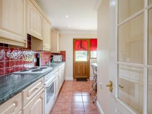 kuchnia z białymi szafkami i czerwoną podłogą wyłożoną kafelkami w obiekcie Appletree Cottage w mieście Saint Osyth