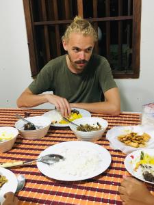 Sweet Pea Hostel في بالابيتييا: رجل يجلس على طاولة مع أطباق من الطعام