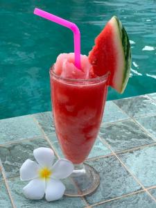 een drankje met een stuk watermeloen en een bloem naast een zwembad bij Khanom Golden Beach Hotel in Khanom