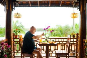 Eco Wooden villa Hoi An في هوي ان: رجل يجلس على طاولة مع طبق من الطعام