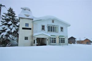 una casa coperta di neve di fronte a un albero di Starfall Lodge a Hakuba