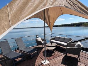 una terraza con sillas, un sofá y una sombrilla en Schwimmende Ferienhäuser auf dem See - Spreewald en Vetschau