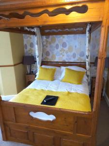 Cama con marco de madera y almohadas amarillas en Virginia Cottage Guest House, en Bowness-on-Windermere