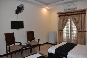ein Schlafzimmer mit einem Bett, 2 Stühlen und einem TV in der Unterkunft Hotel de Raj Sialkot in Sialkot