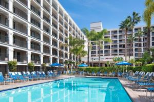 einem Pool mit Stühlen und Sonnenschirmen vor einem Gebäude in der Unterkunft Fairfield by Marriott Anaheim Resort in Anaheim