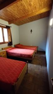 two beds in a room with red sheets and wooden ceilings at Casa en Tafí del Valle in Tafí del Valle