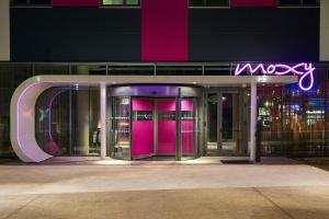 einen Eingang zu einem Gebäude mit rosa Türen und einem Neonschild in der Unterkunft Moxy Paris Charles de Gaulle Airport in Roissy-en-France