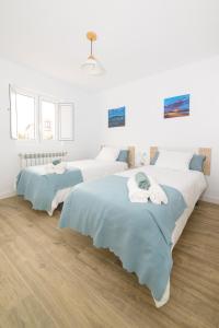 twee bedden in een kamer met witte muren en houten vloeren bij Apartamentos turísticos Praia de Seselle, terraza y jardín a un paso de la playa in Ares