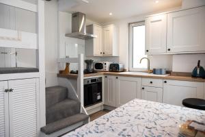 a small kitchen with white cabinets and a staircase at Sandals cottage in St Ives +16 photos