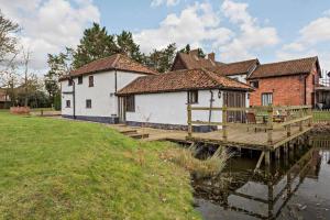 a house on a dock next to a body of water at PondView Cottage with swimming pool, and garden in Tibenham