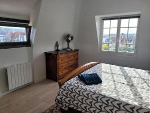 a bedroom with a bed and a dresser and two windows at Les Embruns - Plein ciel - appartement 3eme étage in Deauville
