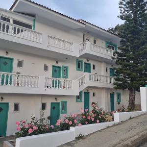 een gebouw met groene en witte deuren en bloemen bij Arocaria - Faliraki peaceful apartments in Faliraki
