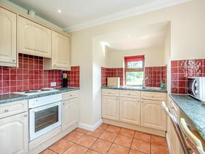 a kitchen with white cabinets and red tiles at Orchard Cottage in Saint Osyth