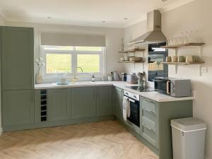 cocina con armarios verdes, fregadero y ventana en Mossdale Cottage en Dalmellington