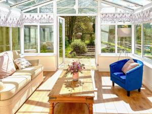 Salón acristalado con sofá, silla azul y mesa en Garden Cottage 1 - Uk42881 en Liphook