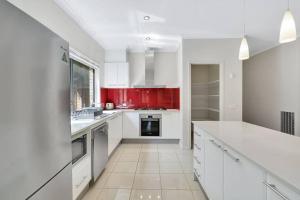 een keuken met witte apparaten en rode kasten bij Spacious 4BR House In Great Location in Point Cook