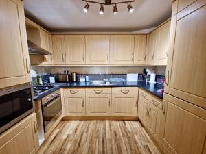 a kitchen with wooden cabinets and black counter tops at Stunning Luxury Serviced Apartment next to City Centre with Free Parking - Contractors & Relocators in Coventry