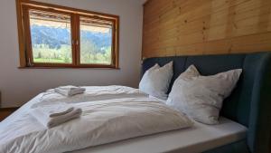 a bed with white sheets and pillows and a window at Idyllisches Berg-Chalet mit Panoramablick in Bayrischzell