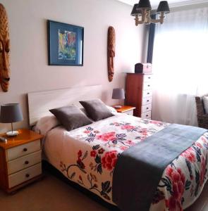 sypialnia z łóżkiem z kwiatową narzutą i komodą w obiekcie Apartamento con jardín Playa Foz w mieście Foz