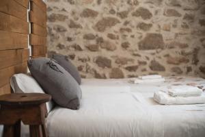 1 cama blanca con almohadas y pared de piedra en El Pajar de Tía María, en Casas del Castañar