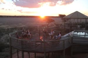 un grupo de personas sentadas alrededor de un fuego al atardecer en Suricate Tented Kalahari Lodge, en Hoachanas