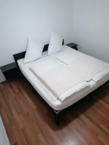 a white bed with two pillows on a wooden floor at Apartma Sandi in Šentilj